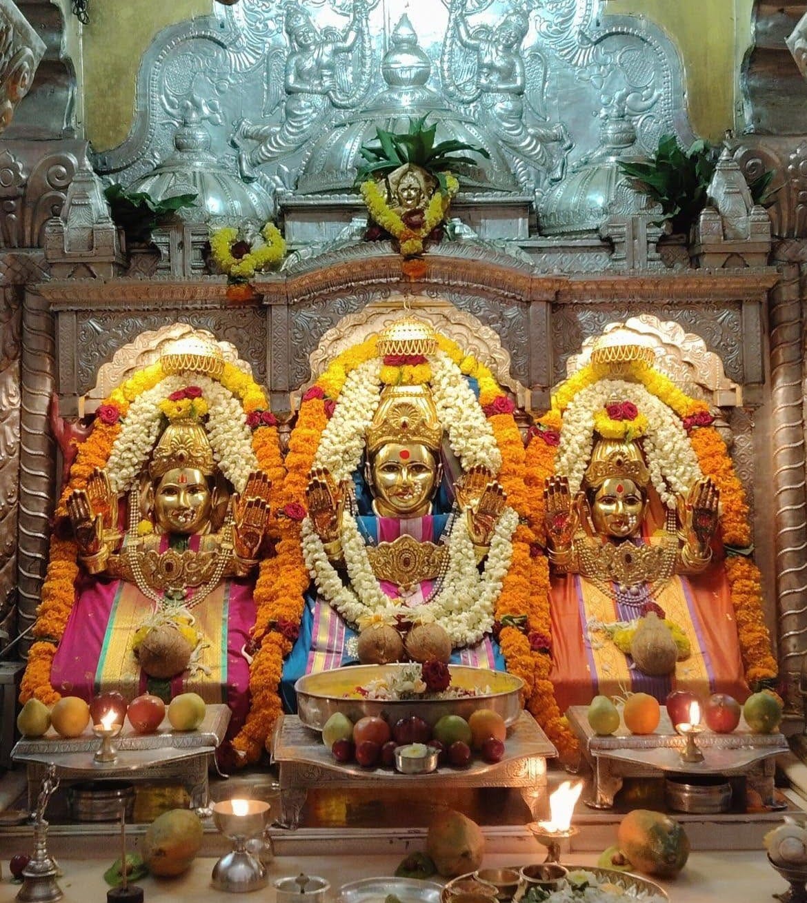 Temple shrine with three deities adorned with marigold garlands and offerings