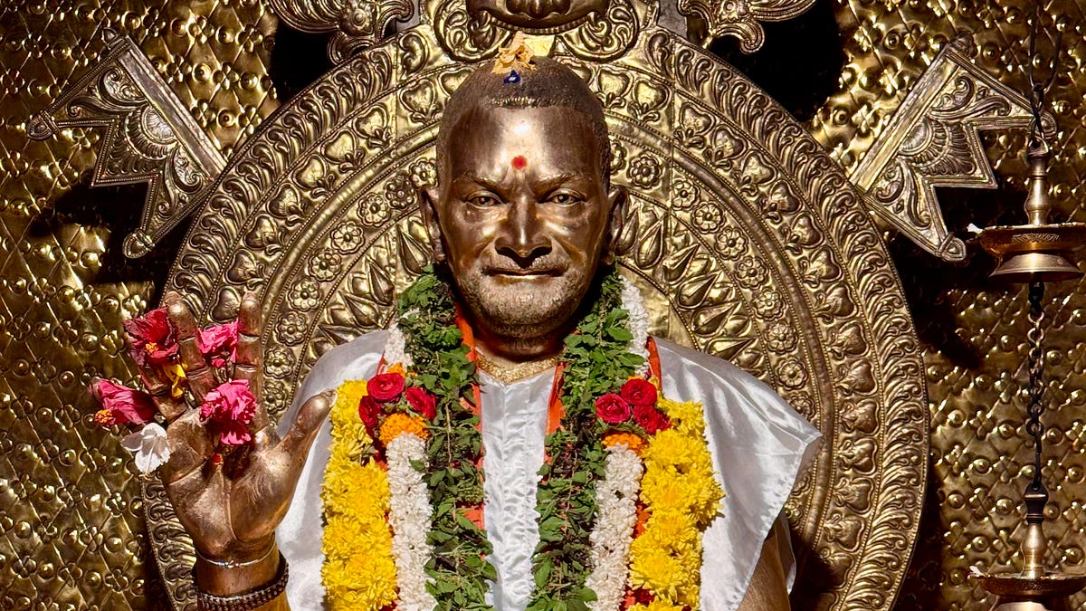 Bronze statue of Bhagawān Nityānanda adorned with flower garlands