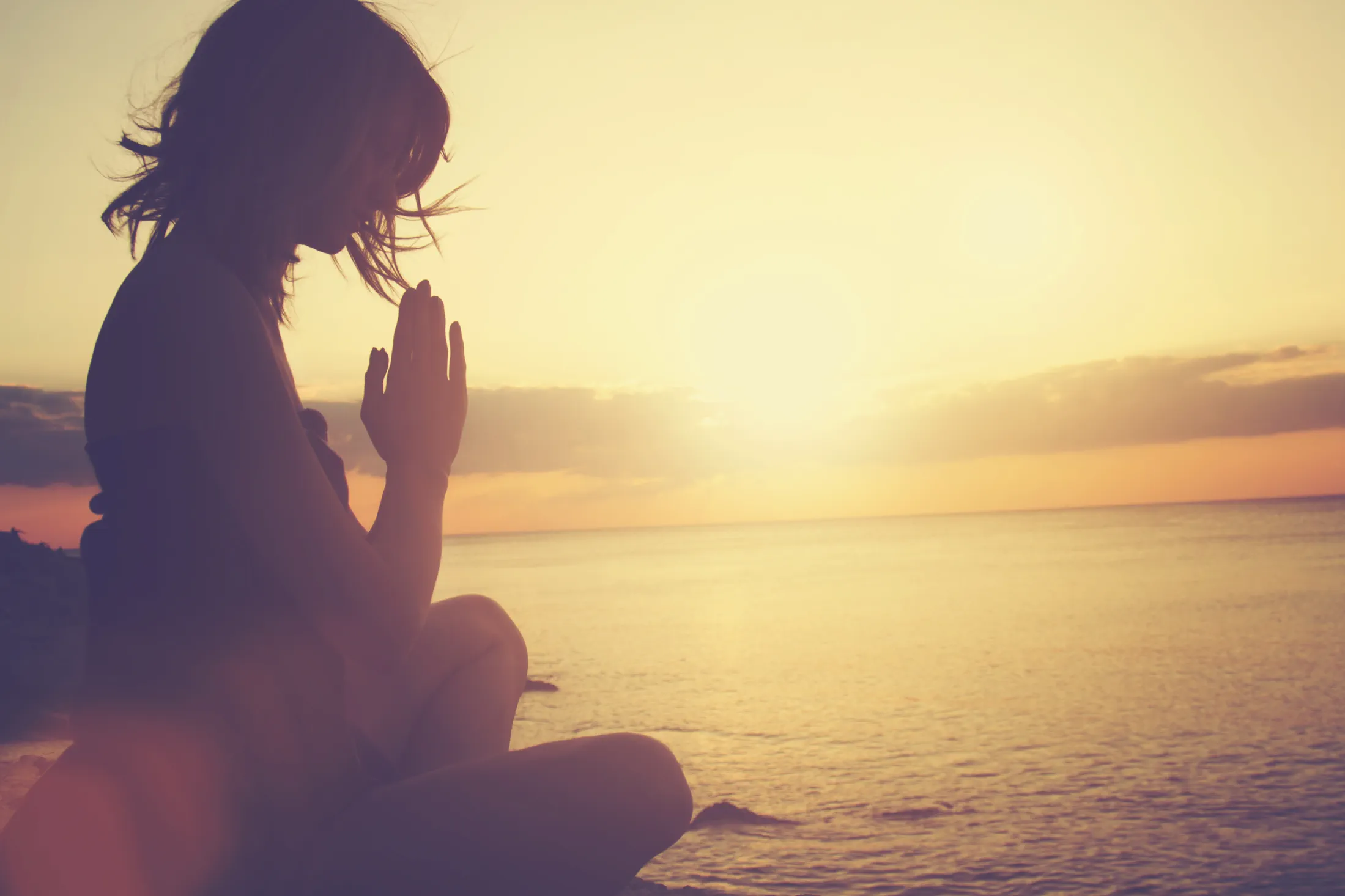 A person meditating beside the sea at sunrise
